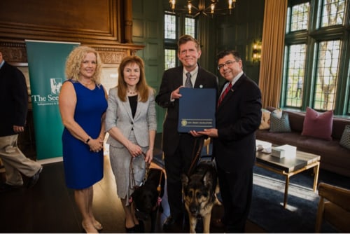 Amy Bucco, Ginger Kutsch, Seeing Eye President & CEO Jim Kutsch and Assemblyman Anthony Bucco pose for a photo with the three proclamations from the state of New Jersey. Ginger’s black Lab and Jim’s German shepherd stand beside them.
