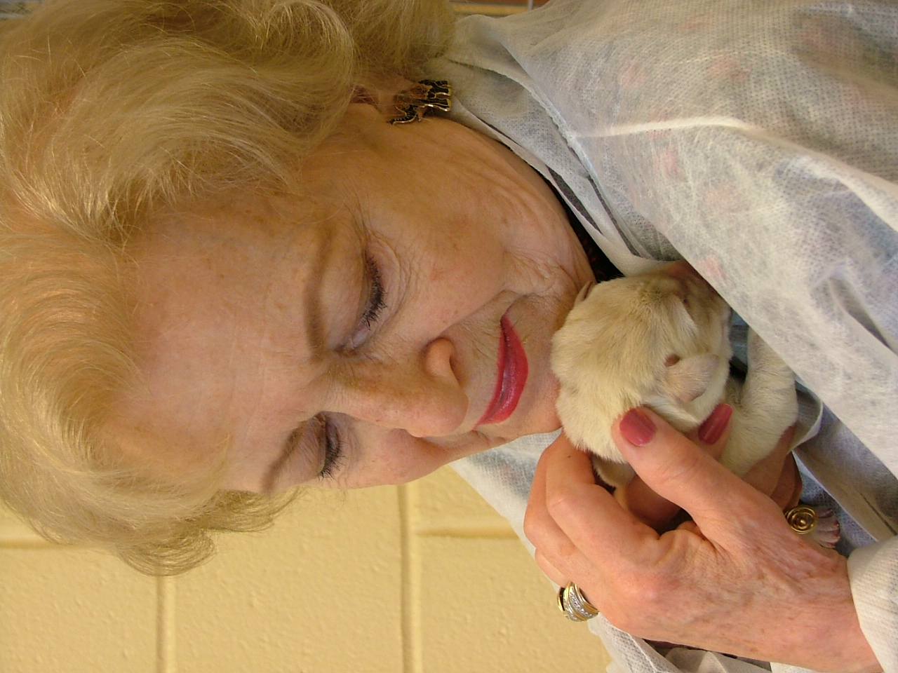 Betty cuddles a newborn yellow Lab to her chest and looks down, smiling as she pets the puppy.