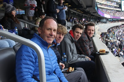 A man smiles with his three grown sons seated beside him in their stadium seats.