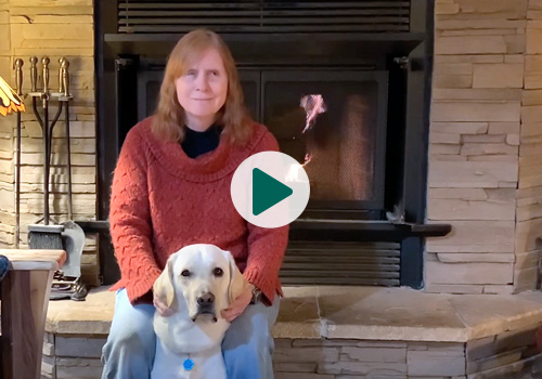Graduate Karen sits in front of a fireplace with her yellow Lab Seeing Eye dog Dave