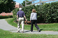 A Seeing Eye instructor holds the body of an empty Seeing Eye harness and guides a student around the turn of a path. 