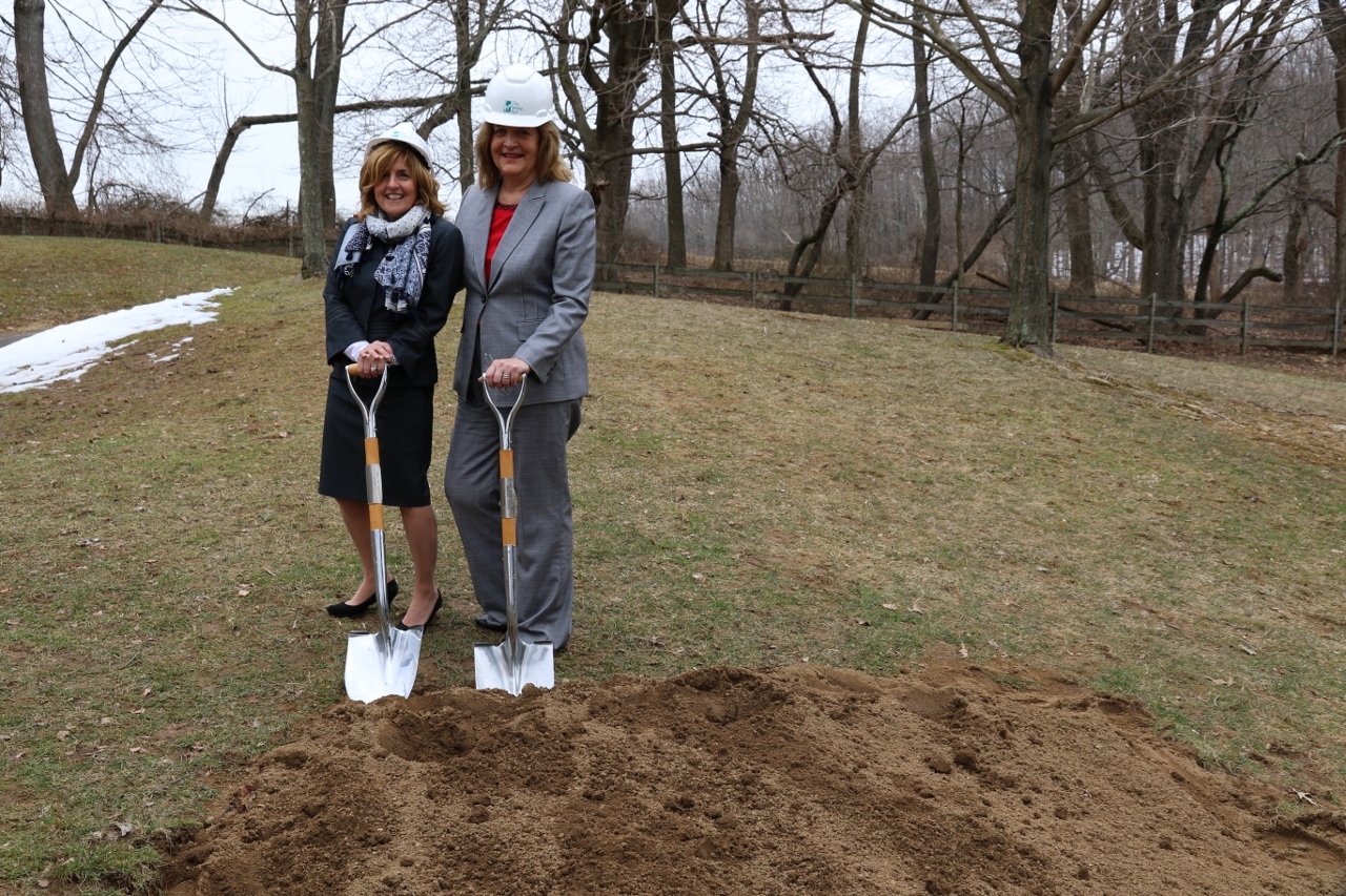 Deb and Dr. Holle smile while holding shovels and wearing hard hats at the site of the groundbreaking. 