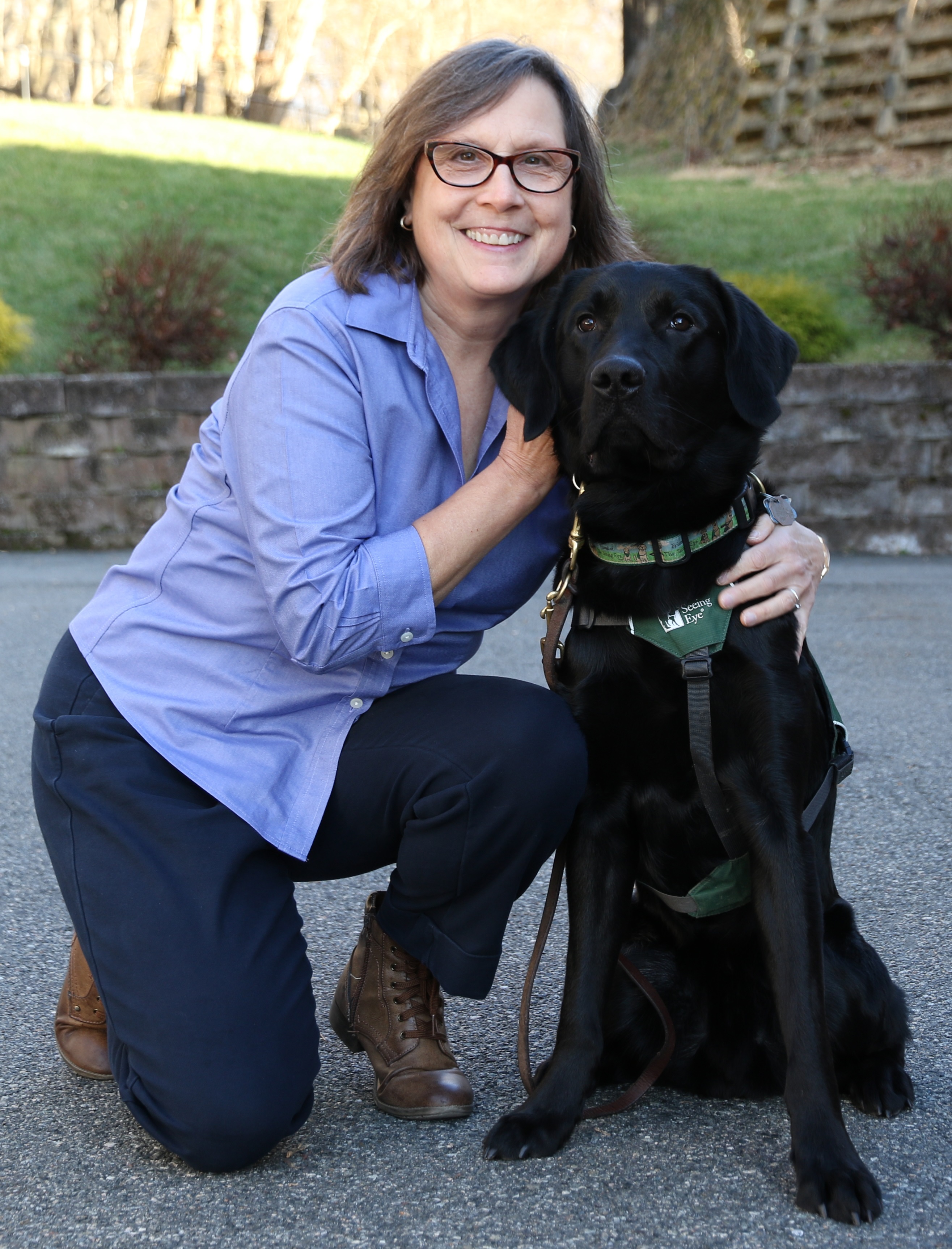Daphne Halpern with a black Labrador/golden retriever cross wearing a green Seeing Eye puppy raiser program vest.