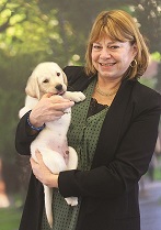 A photo of Peggi Howard holding a small yellow Labrador retriever puppy.