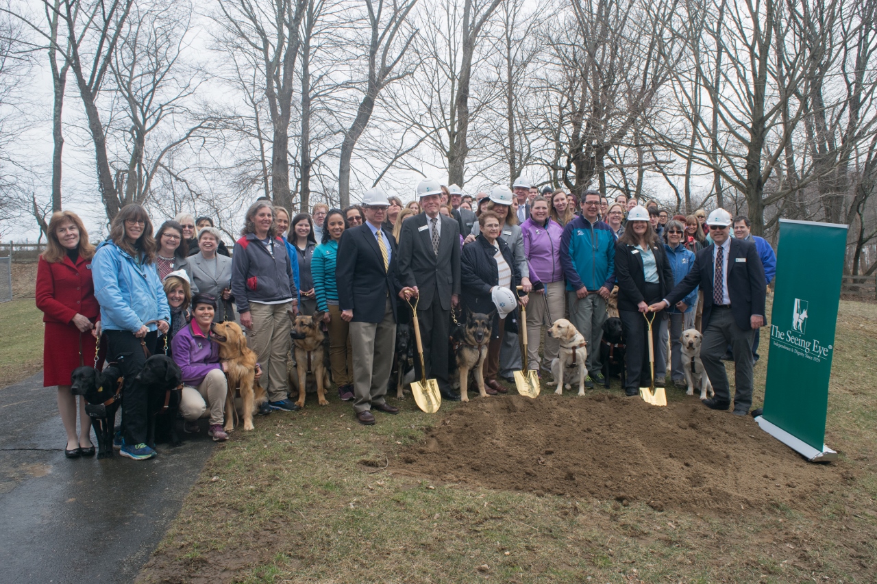A crowd of Seeing Eye staff stand for a photo at the groundbreaking site which is a patch of earth at the edge of the property next to the Vincent H. Stabile Canine Health Center. 